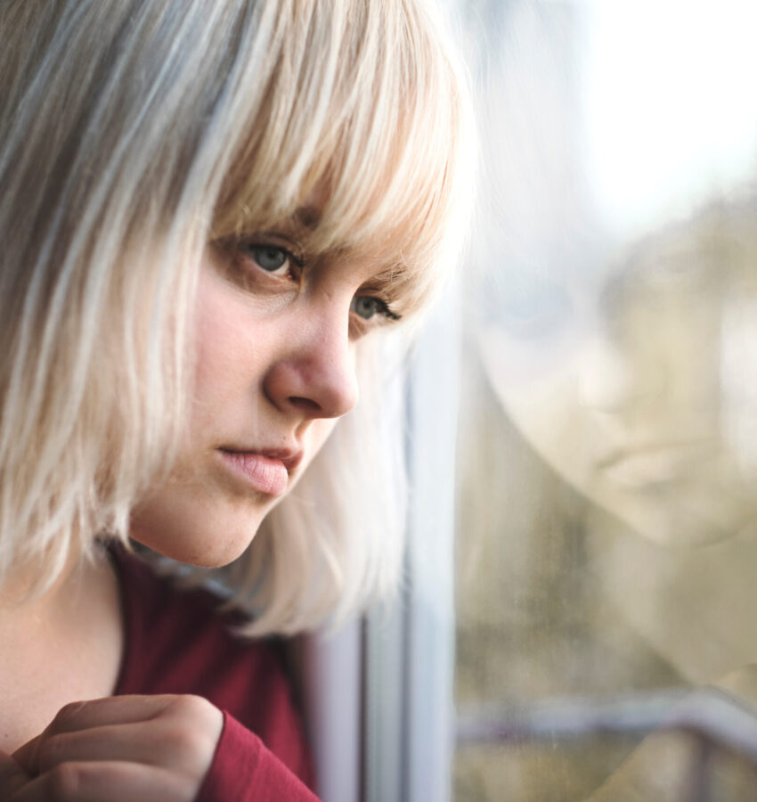 Close up of depressed young blond woman near window at home. Sa Close up of depressed young blond woman near window at home. Sa