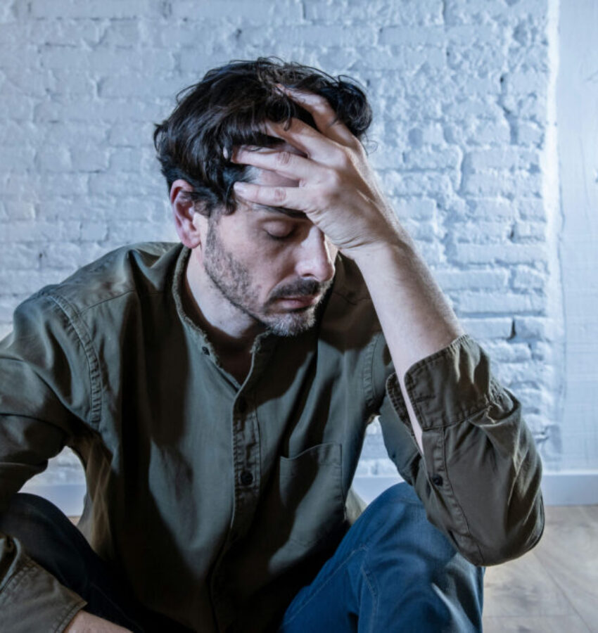 a man sits on the floor, hands on his head, needing treatment for schizophrenia